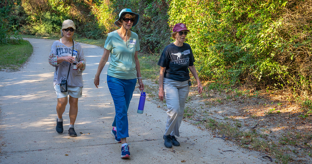 three senior women walking on a park trail