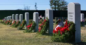 line of gravestones with holiday wreaths resting on each.