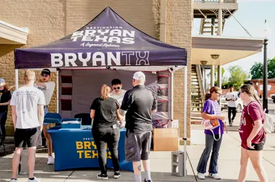 Destination Bryan market booth with logos and interested attendees surrounding the booth.