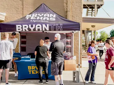 Destination Bryan market booth with logos and interested attendees surrounding the booth.