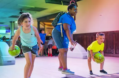 young girl and boy excited to bowl while a supportive camp counselor encourages them