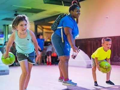 young girl and boy excited to bowl while a supportive camp counselor encourages them