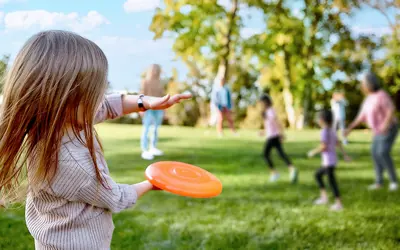 young girl in the foreground throwing a frisbee to family members in an outdoor park while others run and play