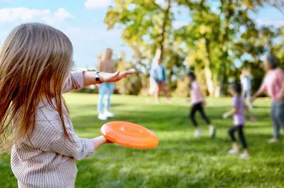 young girl in the foreground throwing a frisbee to family members in an outdoor park while others run and play