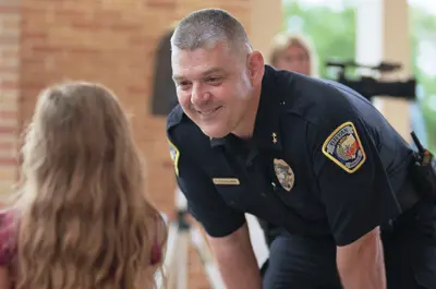 officer leaning down and smiling while greeting a child at a community event