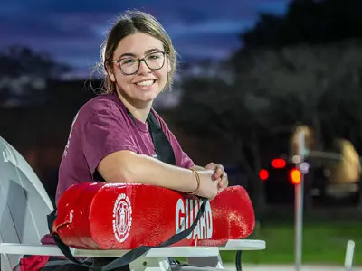 Lifeguard sitting in a lifeguard chair smiles at the camera.