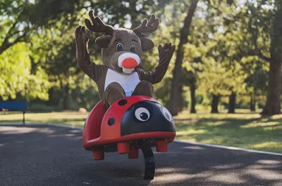 A reindeer mascot rides a ladybug spring rider at a park.