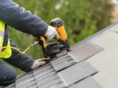 Roofer using a nail gun to nail down shingles.