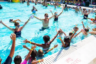 instructors in the pool teaching a swimming lesson to a group of children of varying ages