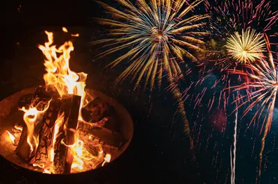 open burn pit fire with fireworks bursting in the background