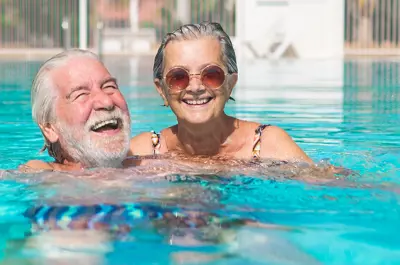 elderly man and woman couple laughing and swimming in the pool on a sunny day