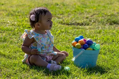 Young girl sits on the grass next to a bucket overflowing with easter eggs.