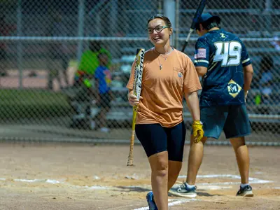young woman laughing and carrying a softball bat after hitting with her male team. mate preparing to hit behind her