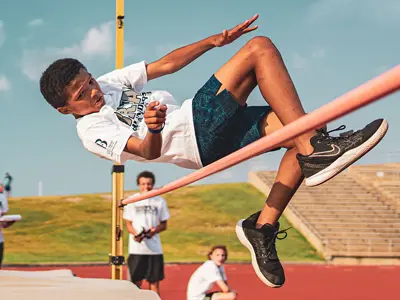 young boy practicing pole vaulting with team mates while wearing a Bryan Thunderbolts t-shirt