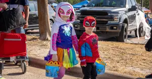 children dressed in superhero costumes carrying buckets to collect candy.