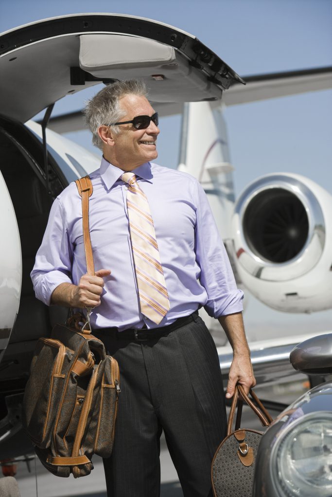 Senior happy businessman standing by airplane with luggage at ai