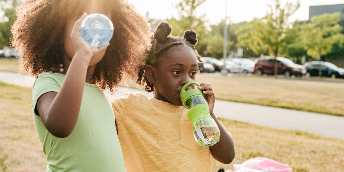 Photo of two girls drinking from water bottles.