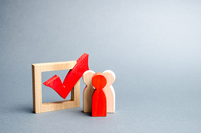 Three wooden meeples standing next to a checkbox