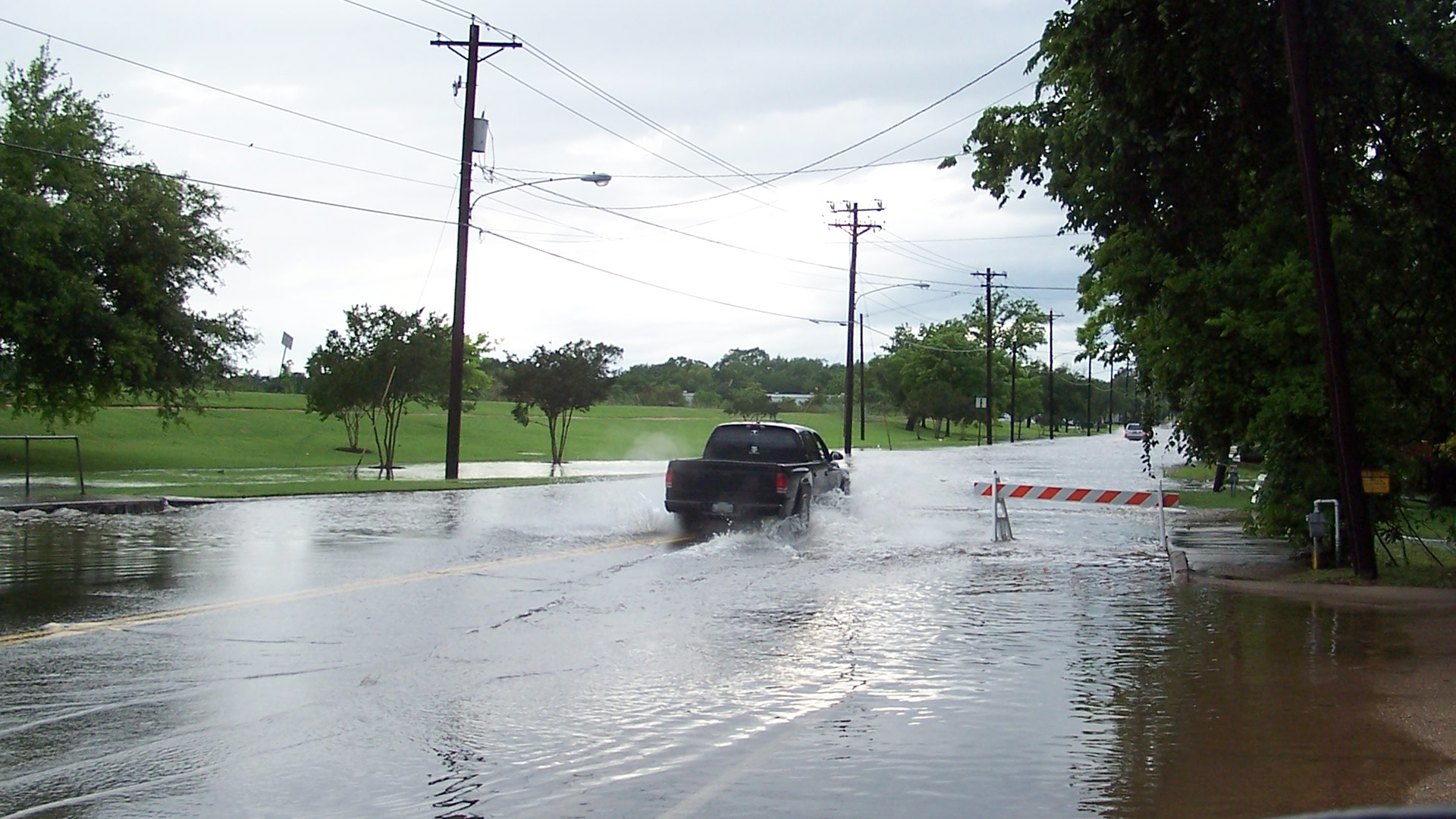 Black truck driving through water over a roadway
