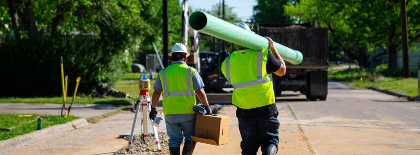 Wastewater workers carrying a new sewer pipe.