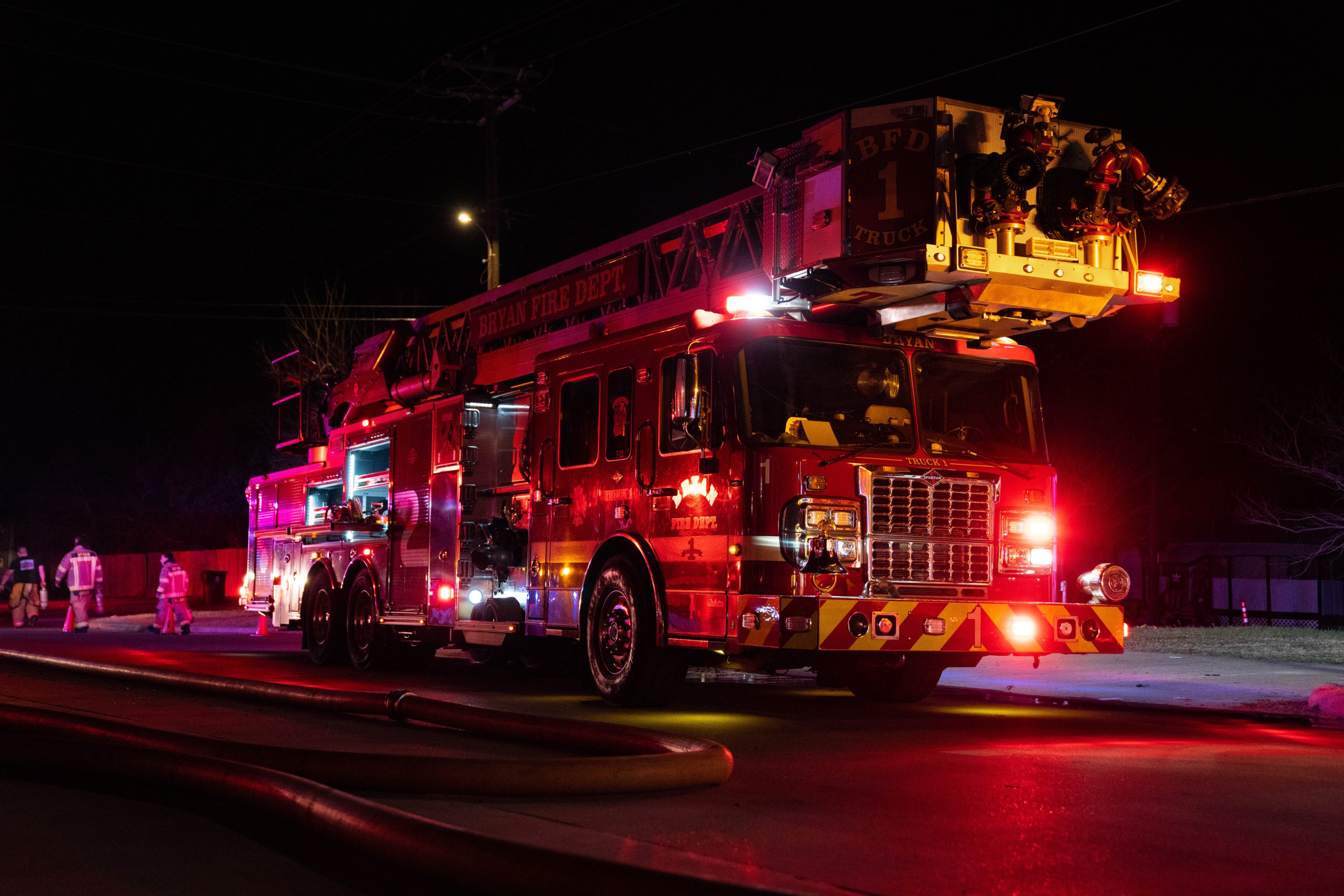 Photo of a Bryan fire truck with lights on at night. Firefighters working in the background.