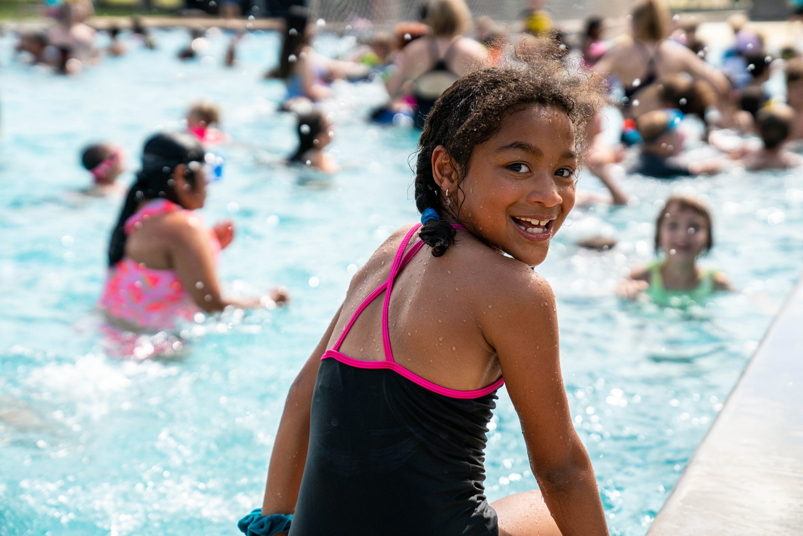 Girl sitting on side of the pool looking at camera and smiling