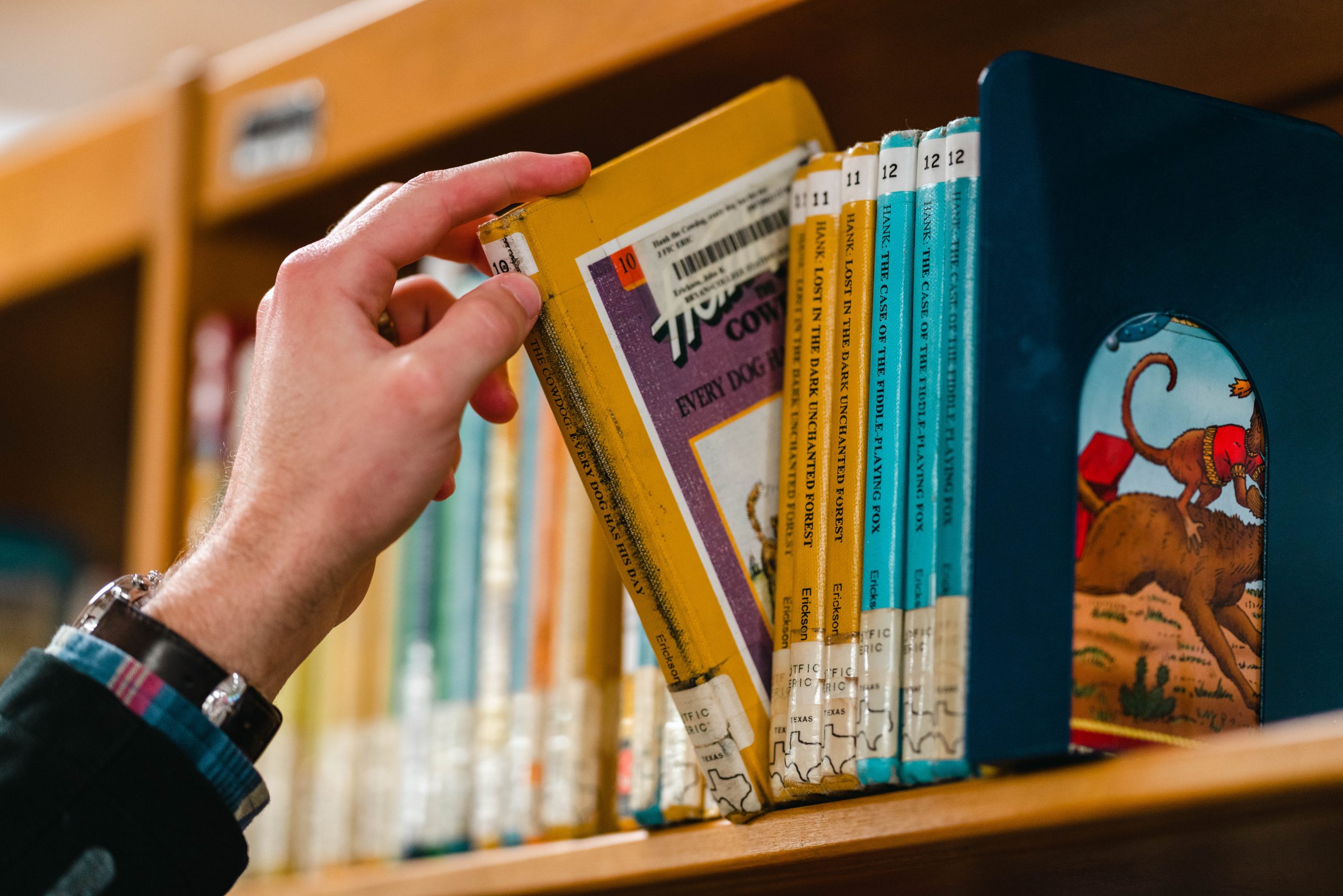 Photo of person taking a book off of a shelf at the library. 