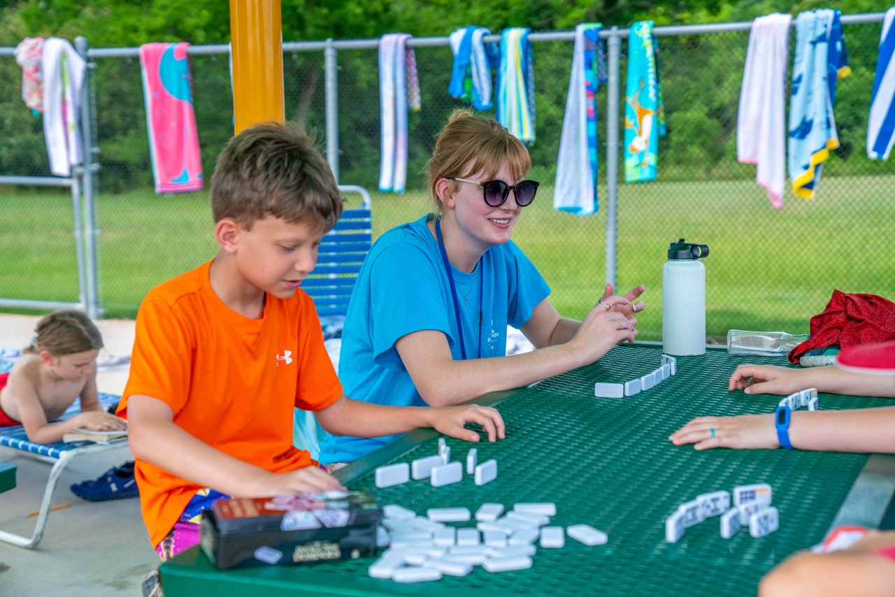 Photo of Camp Counselor playing dominoes with campers. 