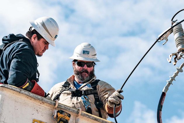 BTU lineworkers inspecting power lines at the top of a power pole.