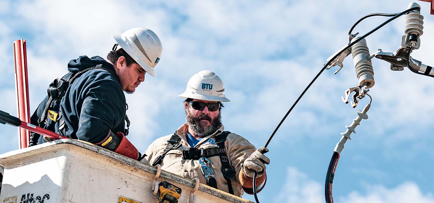 BTU lineworkers inspecting power lines at the top of a power pole.