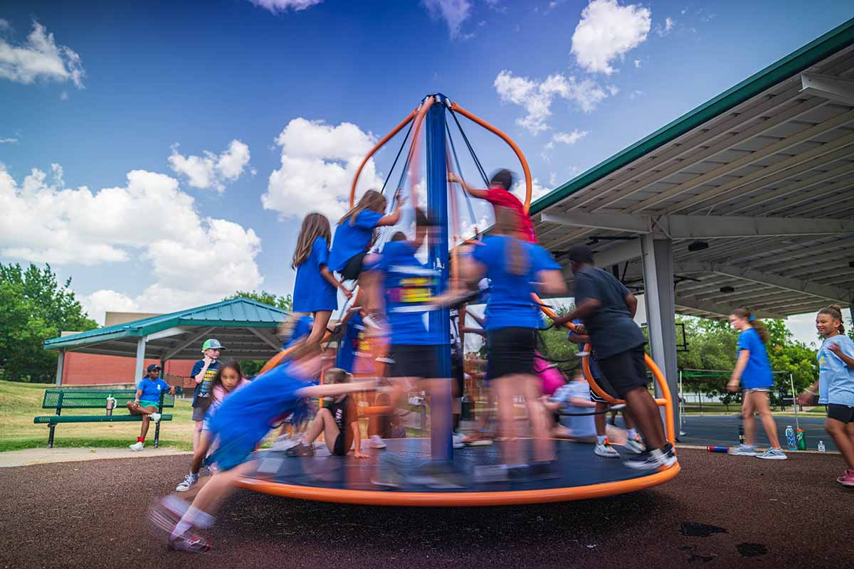 Many children climb onto a playground merry-go-round at Neal Recreation Center in Bryan. They kids are spinning so fast that the photo is blurred with their motion.