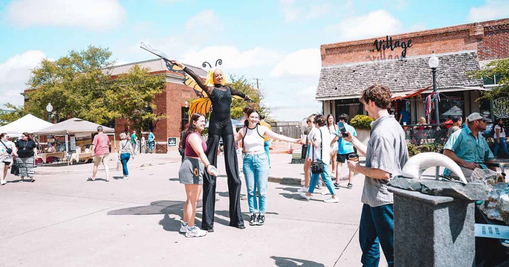 A performance artist on stilts poses for a picture with two young ladies at the Downtown Bryan Street and Art Fair in 2023.