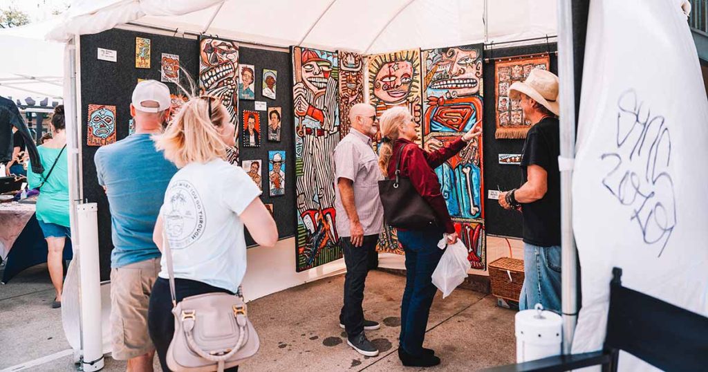 An artists showcases his artwork to 2 men and 2 women at the Downtown Bryan Street and Art Fair in 2023.