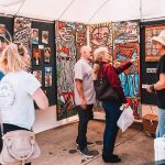 An artists showcases his artwork to 2 men and 2 women at the Downtown Bryan Street and Art Fair in 2023.