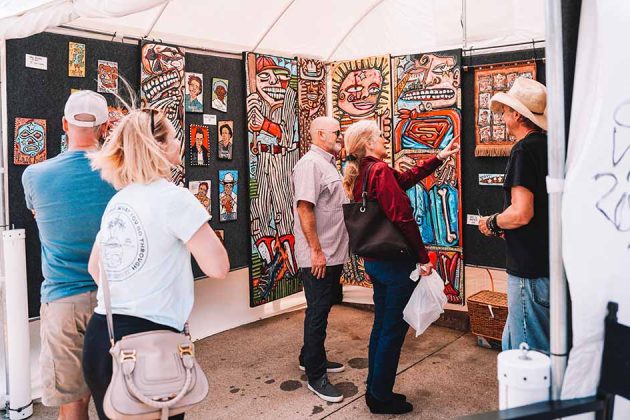 An artists showcases his artwork to 2 men and 2 women at the Downtown Bryan Street and Art Fair in 2023.