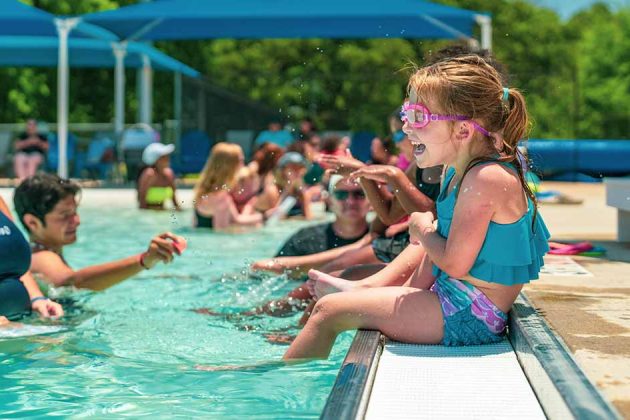 A small girl sits on the side of the pool laughing during a swim lesson at the Bryan Aquatic Center.