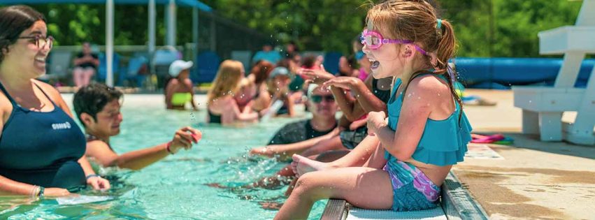 A small girl sits on the side of the pool laughing during a swim lesson at the Bryan Aquatic Center.