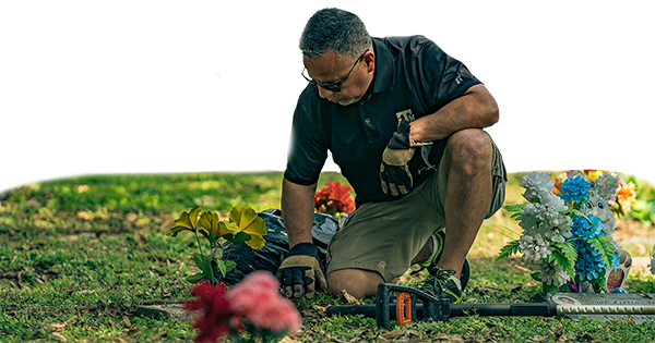 A man kneels down by a grave marker in Bryan City Cemetery and cleans away grass, leaves and debris during a cemetery cleanup day.