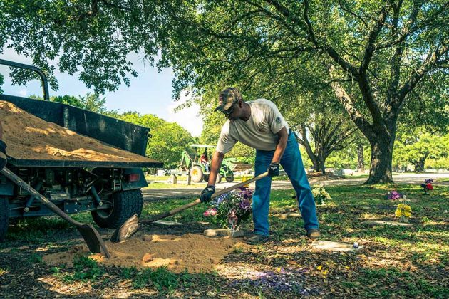 Two men spread filler dirt next to a grave marker in Bryan City Cemetery during a cemetery cleanup day.