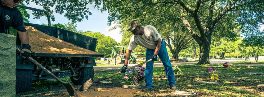 Two men spread filler dirt next to a grave marker in Bryan City Cemetery during a cemetery cleanup day.