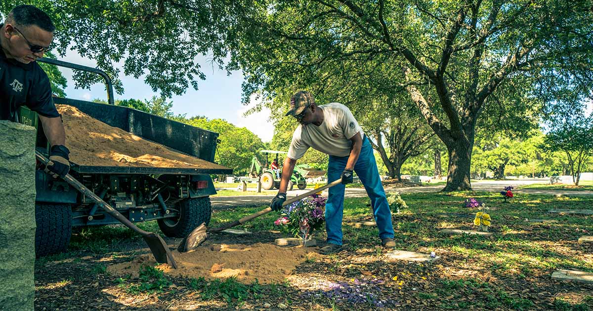 Two men spread filler dirt next to a grave marker in Bryan City Cemetery during a cemetery cleanup day.