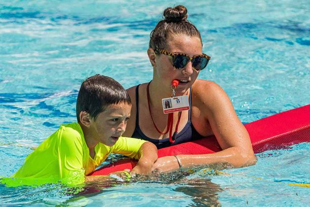 A lifeguard teaches a young boy how to swim.