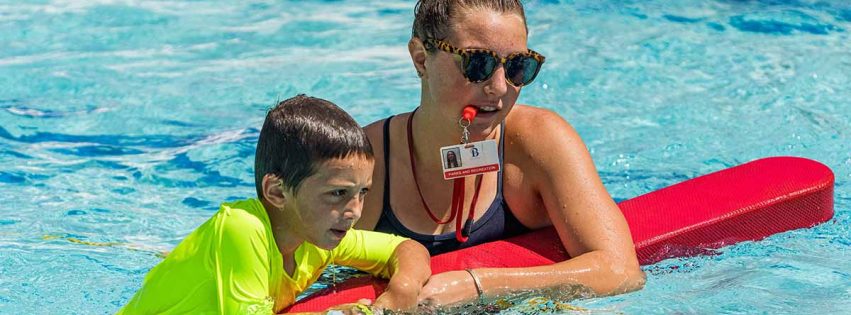 A lifeguard teaches a young boy how to swim.