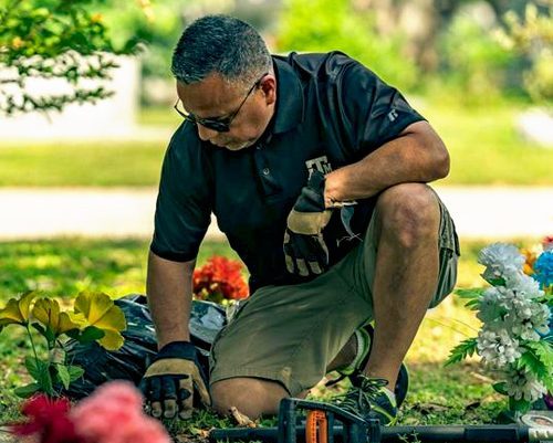 man kneeling and cleaning dirt from a headstone in a cemetery