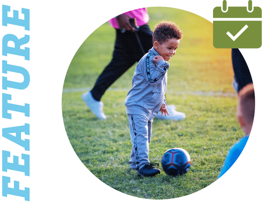 Feature: child kicking a soccer ball on a field with other children