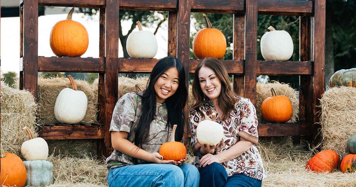 two girls on hay bales holding pumpkins in front of a pumpkin backdrop
